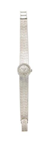 A Lady's gold and diamond Deville cocktail wristwatch, Omega, circa 1960's. Manual. 18mm. Circular case with silver dial and applied baton numerals, diamond set bezel. Case, dial, movement and integral bracelet signed. Weight 36.9 grams. Length 16mm. 