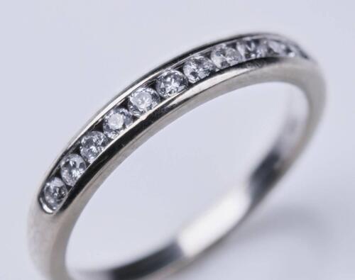 A diamond band ring, the front section channel set with twelve round brilliant diamonds. 10ct white gold. Weight 1.68 grams. Size K. Gemmologist's report available.