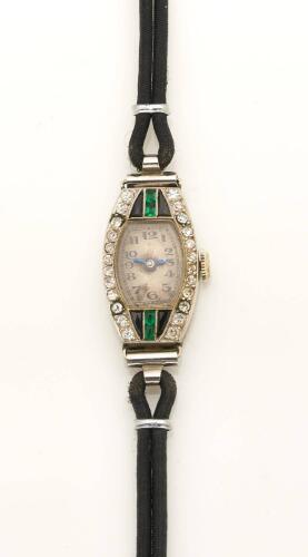 A Lady's Art Deco emerald diamond and onyx wristwatch, circa 1920's. 18mm. Tonneau shaped case set with single cut diamonds and calibre emeralds and onyx. Black strap. 18ct yellow and white gold. Please note: orginal movement has been replaced with quartz