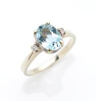 An aquamarine and diamond ring, the central oval aquamarine set either side with a small round brilliant cut diamond. 9ct yellow and white gold. Weight 2.49 grams. Size J.