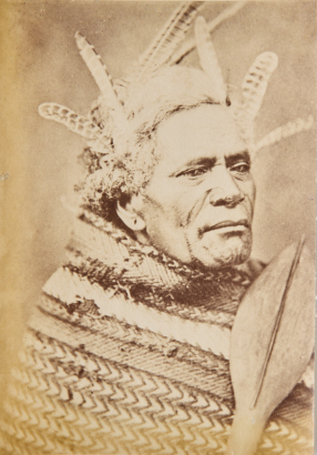 BURTON BROTHERS Unidentified Māori man with feathers in his hair holding a paddle and wearing a whatu kākahu