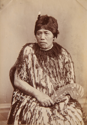 PULMAN'S PHOTOGRAPHIC STUDIO A head and shoulders portrait of a Mere Awhitu, wife of the King's son, with a moko kauae, "Te Rata" arm tattoo, a feather in her hair, a patu and wearing a korowai