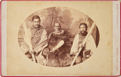 HARRY CECIL TURNER A studio group portrait of three sitters in cloaks with Māori style props infront of a painted scenic backdrop.