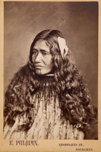 PULMAN'S PHOTOGRAPHIC STUDIO Portrait of a Māori wahine with a feather in her long hair and wearing a korowai