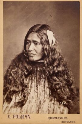 PULMAN'S PHOTOGRAPHIC STUDIO Portrait of a Māori wahine with a feather in her long hair and wearing a korowai