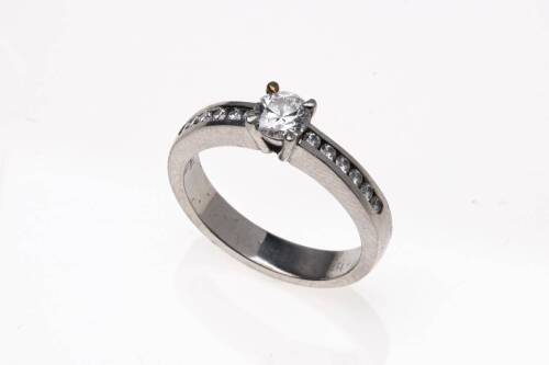 A diamond ring, claw set round brilliant cut diamond centre of estimated weight 0.34 carat, six channel set round brilliant cut diamonds down each shoulder of estimated total weight 0.20 carats. Platinum. Weight 5.5 grams. Size J.