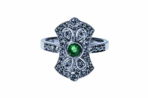 An emerald and diamond plaque ring, the pierced plaque is set with a round cut emerald centre with small round brilliant cut diamonds. 18ct white gold. Weight 6.4 grams. Size M.