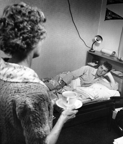 Landlady Vivian Warren takes early morning tea and the newspaper to a tousled Peter Snell, 1962