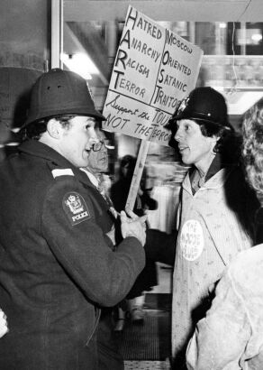 A protester dressed as a police officer is reprimanded by a real police officer during a march in Auckland