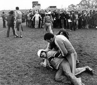 A plainclothes police officer arrests a protester on the field