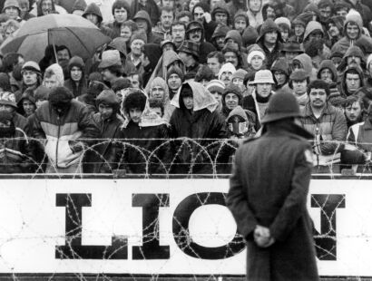 Protesters stand and watch the match unfold behind barbed wire