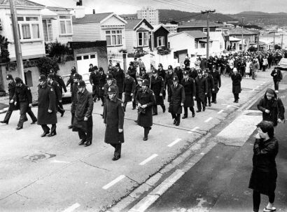 Police officers march in formation down a residential street amid demonstrators