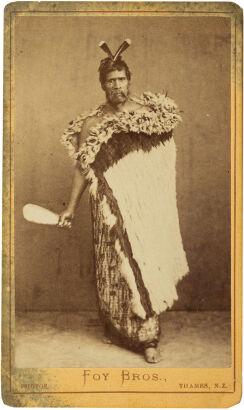 FOY BROS, THAMES Māori man with feathered and korowai cloaks, holding a mere