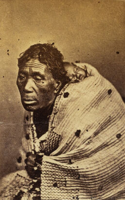 FOY BROS / ELIZABETH PULMAN, THAMES Portrait of Māori woman with sleeping baby on her back wrapped in korowai