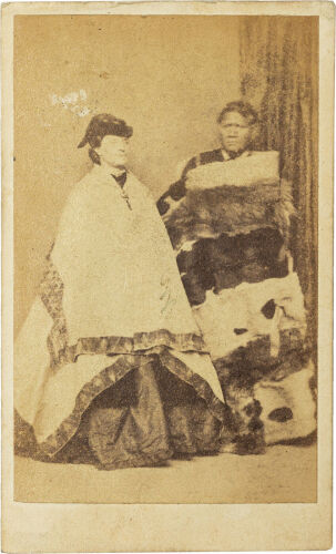 UNKNOWN PHOTOGRAPHER Full length portrait of a European woman in Victorian dress and Kaitaka cloak with Māori man in suit with full length cloak of various skins