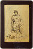 UNKNOWN PHOTOGRAPHER Portrait of Māori man in pake and woven skirt with taniko border, holding taiaha. White feathers in hair.