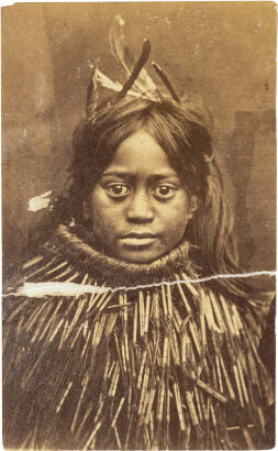 UNKNOWN PHOTOGRAPHER Portrait of a Māori girl with feathers in her hair and piupiu cloak