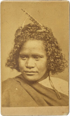 UNKNOWN PHOTOGRAPHER Portrait of a Māori girl with feathers in her hair, ribbon earring and blanket cape