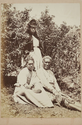 UNKNOWN PHOTOGRAPHER Photograph in garden of two young Māori woman in Victorian dress and Maori man in blanket skirt