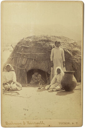 BUCHMANN AND HEARTWELL, TUSCON Tohono O'odham women and girls in front of wickiup brush dwelling with storage pot, Southwest Arizona