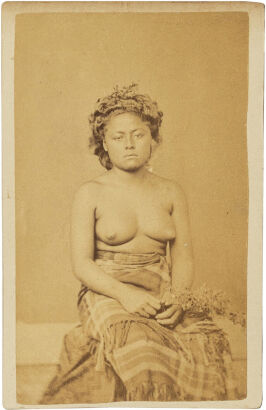 UNKNOWN PHOTOGRAPHER Samoan/Tongan woman seated in blanket skirt on a hwat, holding a stem of flowers