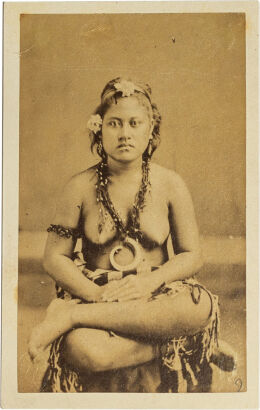 UNKNOWN PHOTOGRAPHER Samoan woman seated cross legged, hair decorated with flowers, wearing earrings, arm bracelet and boar tusk on woven necklace