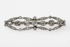 An Edwardian diamond brooch, the line of seven round and cushion shaped old cut diamonds within a border of rose and old cut diamond leaves with milled edges. Length 47mm. Aberdeen box.