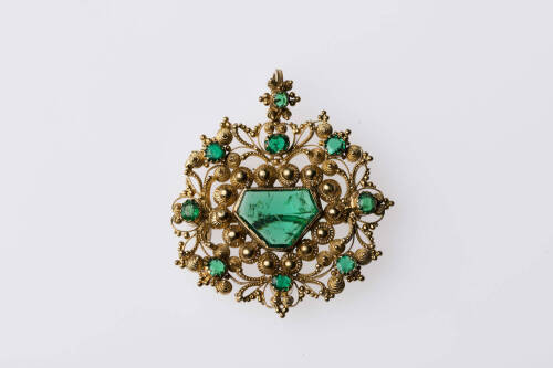 An emerald and gold pendant, the trapezoid shape emerald 12mm x 9mm  Designed in circular form of open canitelle scrolls with eight small surrounding emeralds. Length 43mm. Weight 10.6 grams. Circa 1840.