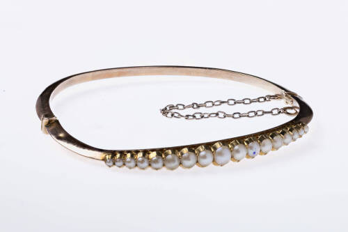 An Edwardian gold and seed pearl bangle, C.1905. Marked 15ct on a tag, the hollow knife edge hinged bangle is set with 17 graduating half seed pearls. Rose gold. Weight 7.34 grams. Inside diameter 5cm. 