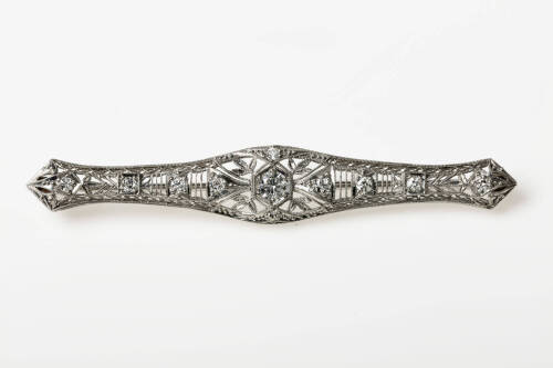 An Art Deco diamond brooch, eleven early brilliant cut diamonds set in a long pierced open work brooch with millgrain edge. Weight 7.0 grams. Length 69mm. Circa 1925.&nbsp;
