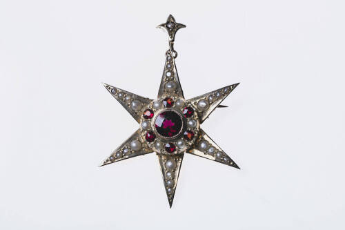 A Victorian garnet and pearl pendant brooch, the six pointed star is bead set with half seed pearls and garnets. 9ct yellow gold. &nbsp;Weight 3.0 grams. Width 37mm. &nbsp;Makers tag J.C.N.