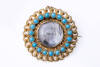 A Victorian turquoise and gold memorium brooch, the target brooch shape with central glassed locket window is surrounded by two borders one with rubover turquoise the outer raised canetille motifs. Diameter 34mm. Circa 1840.