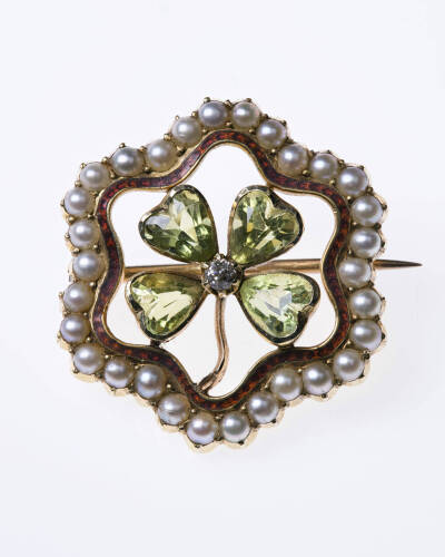 An Edwardian peridot and pearl brooch, four heart shape peridots around a central old cut diamond with shaped seed pearl border. 15ct rose gold. &nbsp;Diameter 22mm.