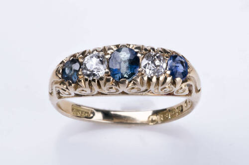 An Edwardian sapphire and diamond bridge ring, the three oval sapphires and two old cut diamonds are claw set in a scroll engraved mount. 18ct yellow gold. Weight 5.34 grams. Size N. Hallmarked Birmingham 1903.&nbsp;