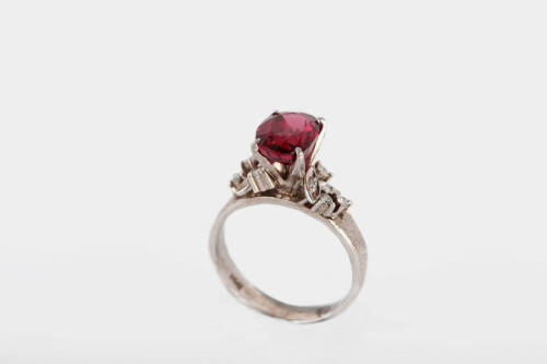 A garnet and diamond ring, the oval purple garnet in a four claw raised setting with five mixed cut diamonds in cluster pattern on each shoulder, on a textured band. 18ct white gold. Weight 4.58gms. Size L.