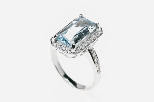 An aquamarine and diamond ring, the central rectangular fancy cut aquamarine of known weight 3.28 carats, four claw set in a diamond frame with diamond set shoulders. Total known diamond weight 0.22 carats. 18ct white gold. Weight 8.7 grams. Size N.