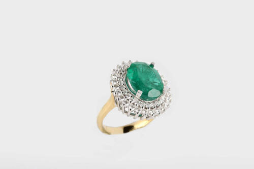 An emerald and diamond ring, the oval emerald measuring 13.6mm x 11.06mm of reported weight 6.65 carats, surrounded by double row of round brilliant cut diamonds of reported total weight 1.28 carats.18ct yellow gold. Weight 11.98 grams. Size N.