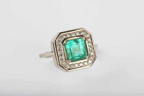 An emerald and diamond ring, the square emerald cut emerald 7.2mm x 6.9mm of estimated weight 1.94 carats surrounded by 24 grain set round brilliant diamonds of estimated weight .32 carats. 14ct white gold. Weight 5.86 grams. Size M.&nbsp;