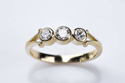 A three stone diamond ring, the bezel set diamonds of estimated total weight 0.28 carat. 18ct yellow gold. Weight 2.56 grams. Size K&frac12;.