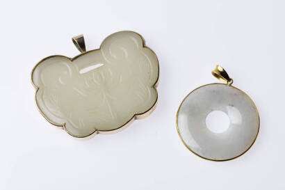 Two jade pendants, the pale green jade of round and lotus designs. 14ct yellow gold. Total weight 59.18 grams. Lengths 52mm and 56mm.