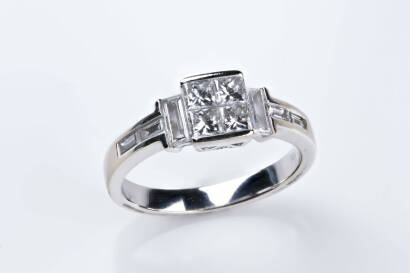 A diamond ring, four princess cut invisible set in a central square design with three baguette diamonds down each shoulder. 18ct white gold. Weight 4.27 grams. Size N.