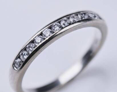 A diamond band ring, the twelve round brilliant diamonds are channel set across front of the band. 10ct white gold. Weight 1.68 grams. Size K.