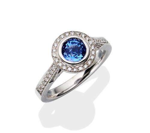 A tanzanite and diamond ring, bezel set with a round tanzanite of known weight 0.97 carat, the mount grain set with forty-eight brilliant cut diamonds of known weight 0.20 carat. 18ct white gold. Weight 5.16 grams. Size M.