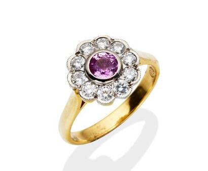 A pink sapphire and diamond cluster ring, bezel set with a central round pink sapphire of known weight 0.60 carat, and surrounded by ten round brilliant cut diamonds of known weight 0.59 carat. 18ct yellow gold. Weight 4.75 grams. Size O&frac12;.