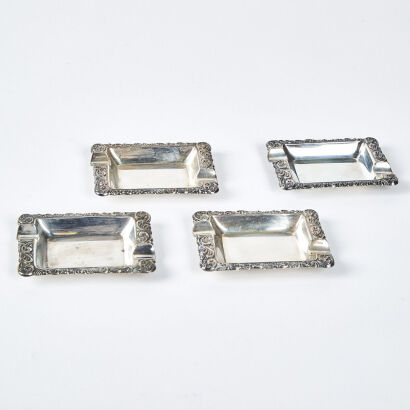 A Set Of Four Silver-Plated Ashtrays With Ornate Border