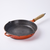 An Orange Cast Iron Frying Pan With Wooden Lid