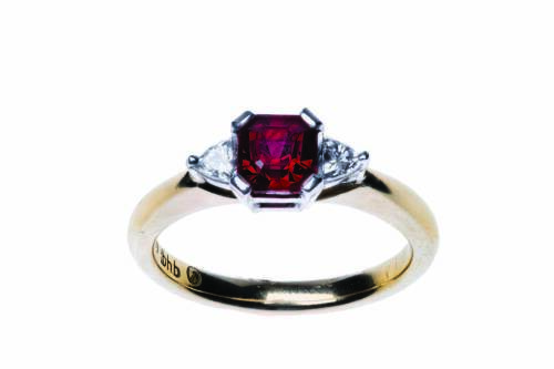 A ruby and diamond ring, four claw set with a square step cut ruby of estimated weight 1.19 carats, set either side with a trilliant diamond of estimated weight 0.10 carat. 18ct yellow gold. Weight 4.60 grams. Size M&frac12;.