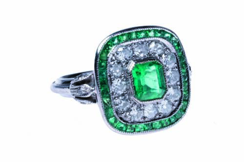 An Art Deco style emerald and diamond ring, the central bezel set rectangular step cut emerald of estimated weight 1 carat, surrounded by a line of twelve old European cut diamonds of estimated weight 0.70 carats and a further line of thirty-two calibre c