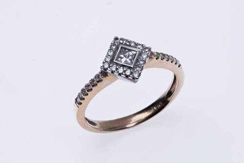 A diamond ring, the central princess cut diamond in an offset square diamond set mount with diamond line shoulders. 9ct rose gold. Weight 2.74 grams. Size N&frac12;..