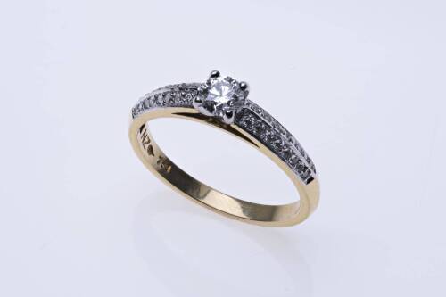 A solitaire diamond ring, four claw with a round brilliant cut diamond and thirty-two small single diamonds set in double rows on either side. 18ct yellow gold. Weight 3.43 grams. Size N.